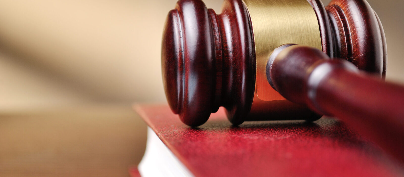 Wooden judges gavel with a brass band around the head resting on top of a closed red law book with shallow dof and copyspace